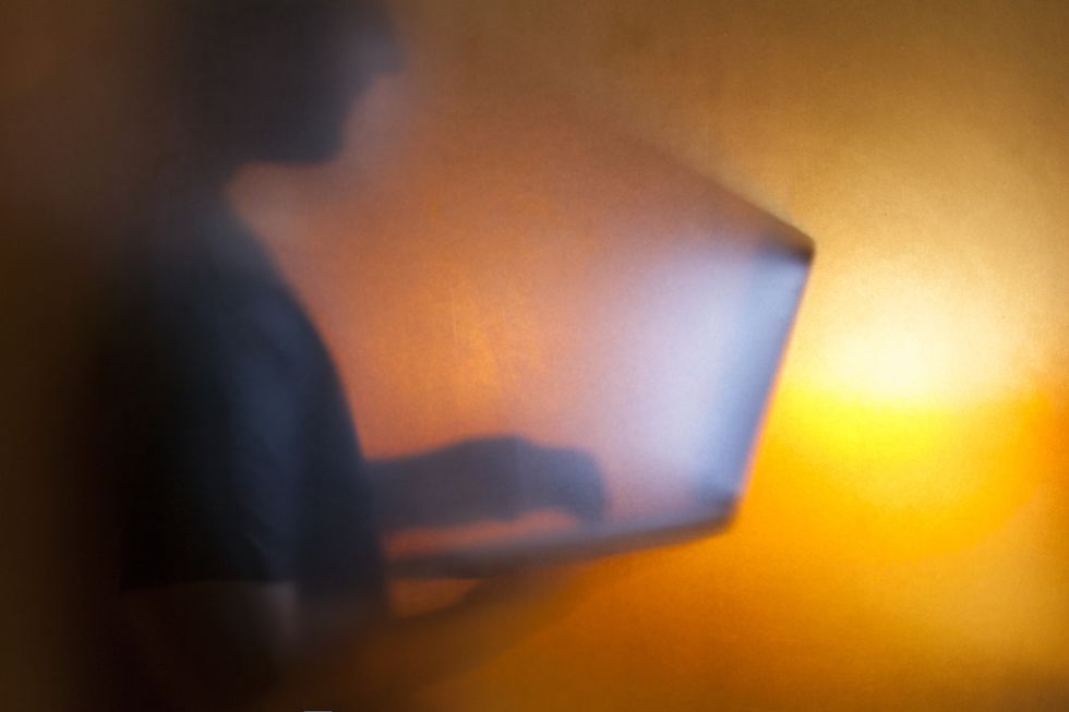 silhouette of man holding computer with light coming out from screen