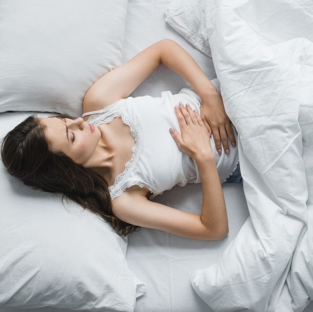 top view of young woman suffering from abdominal pain while lying in bed