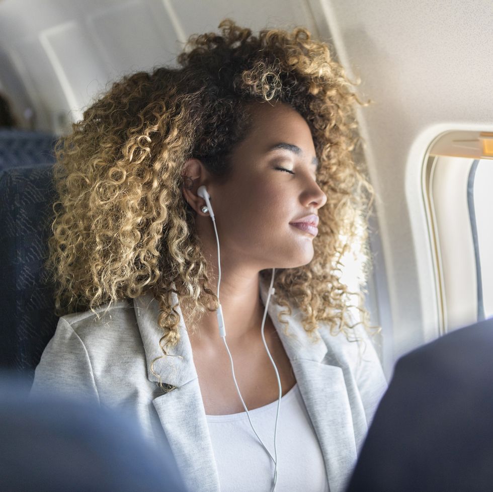 attractive young woman naps during long airplane flight she is wearing earbuds