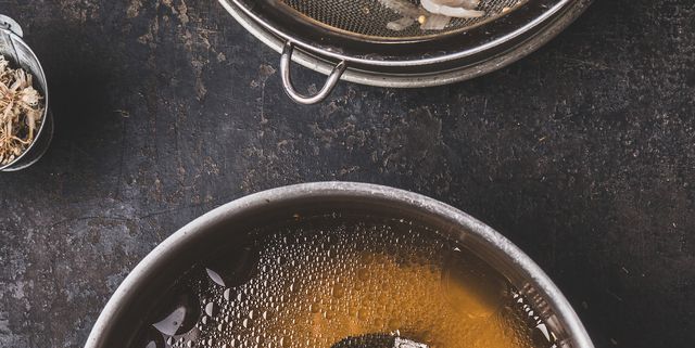 slow cooked clear beef bone broth or stock without meat in cooking pot on dark rustic background, top view step by step
