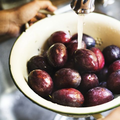 organic plums being washed under running water food photography recipe idea