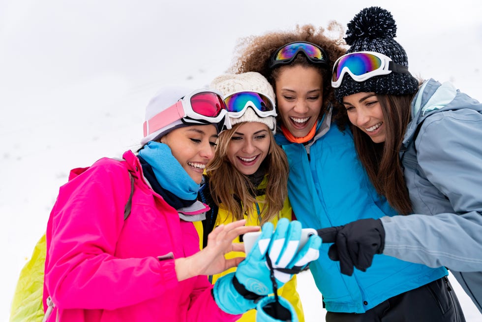 portrait of a group of women in a ski trip looking at social media on a cell phone and smiling