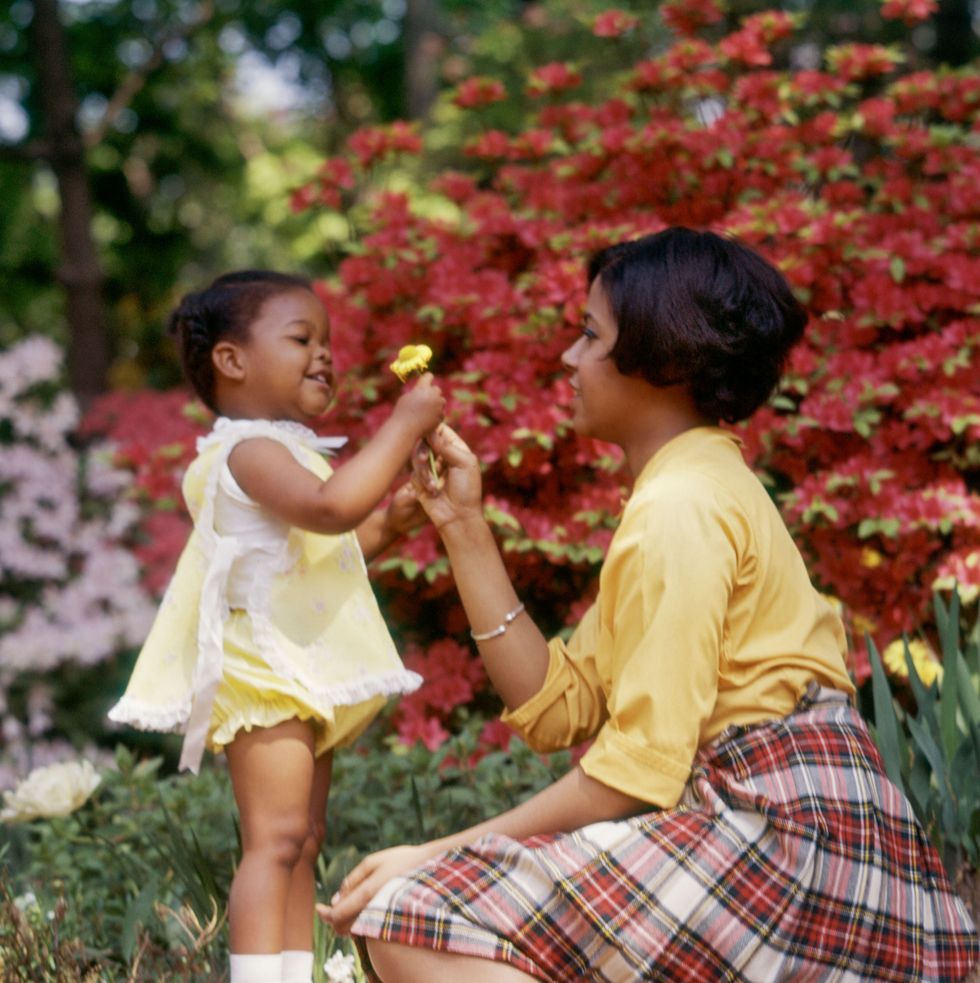 1970s smiling african american woman and little girl outdoors near spring flowers daughter giving yellow flower to mother photo by photo mediaclassicstockgetty images