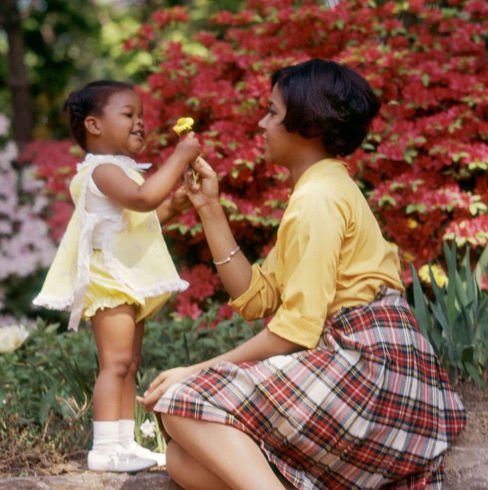 1970s smiling african american woman and little girl outdoors near spring flowers daughter giving yellow flower to mother photo by photo mediaclassicstockgetty images