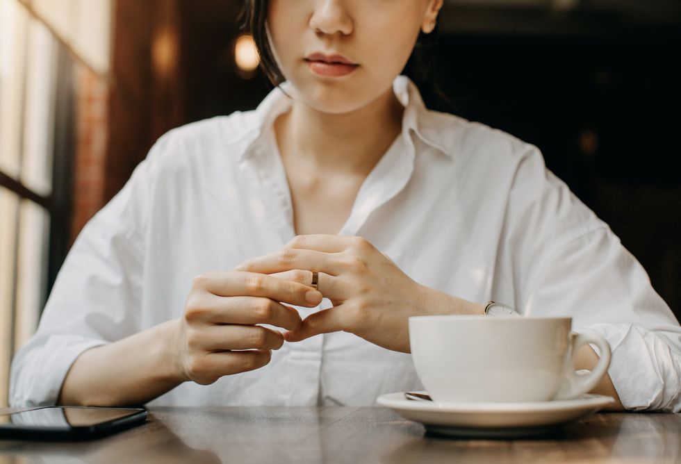 woman touching the wedding ring on her finger nervously while having coffee and waiting in cafe