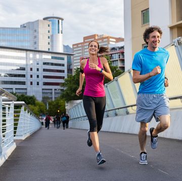 happy man and beautiful woman jogging together city bridge healthy couple running on the city street middle aged couple running with building in the background