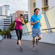 happy man and beautiful woman jogging together city bridge healthy couple running on the city street middle aged couple running with building in the background