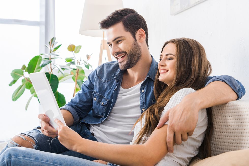 laughing young couple sitting on couch with digital tablet at home
