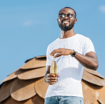 smiling handsome african american man opening soda bottle against blue sky