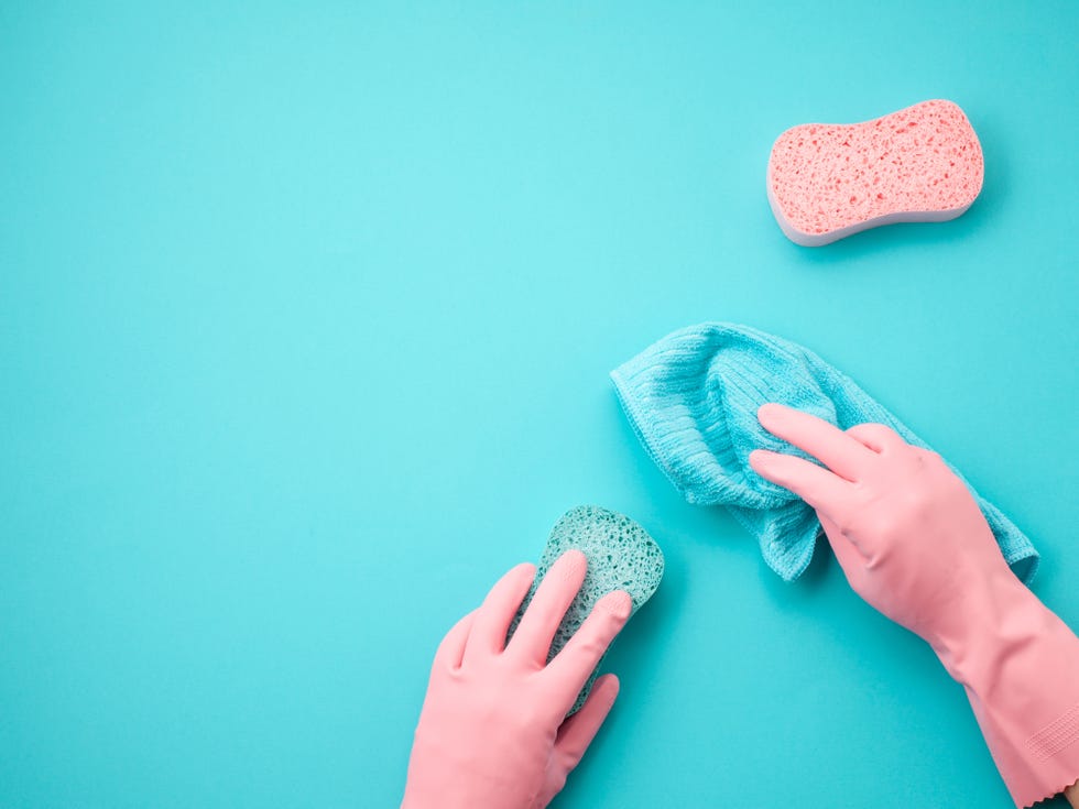 the arms of a person wearing pink rubber gloves and holding two cloths cleaning a blue surface