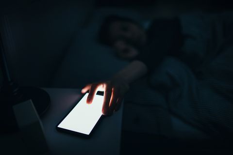 woman reaching and switching off disturbing calls from work on smartphone while sleeping at midnight