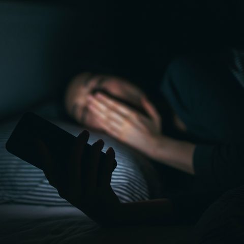 Tired woman yawning while using mobile phone on bed at night