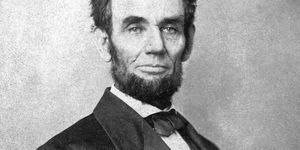 abraham lincoln stars at the camera, he wears a dark colored tuxedo and has a full beard