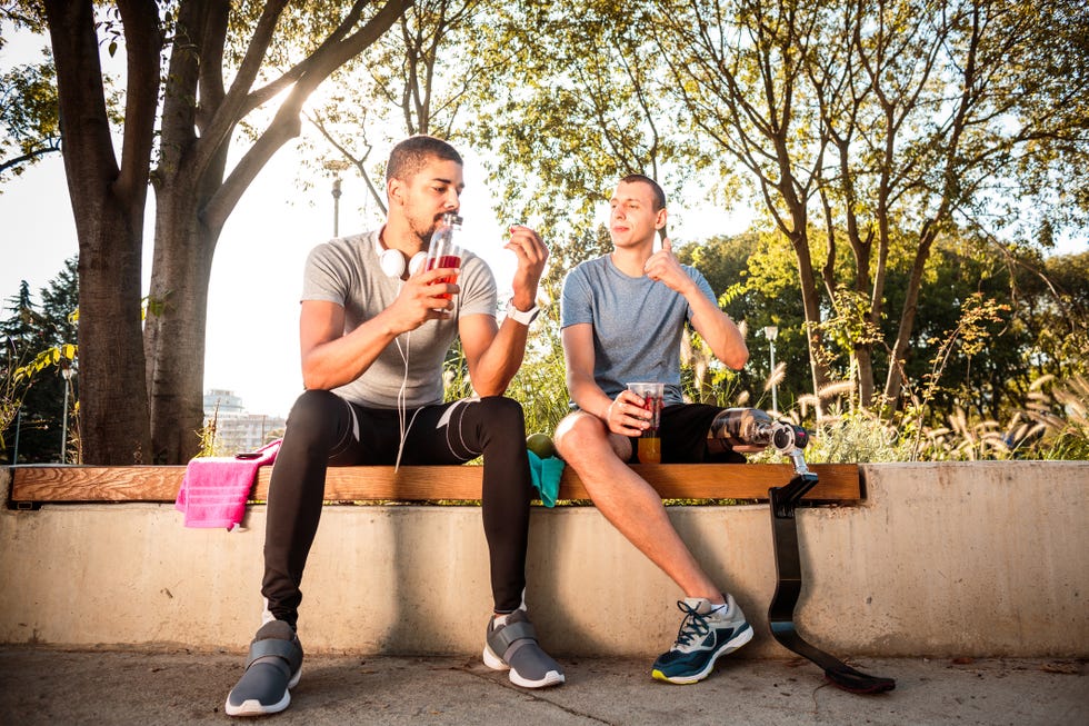 multi ethnic male friends resting and eating berry fruits after training session one of them has prosthetic leg and the other is wearing headphones and smart watch