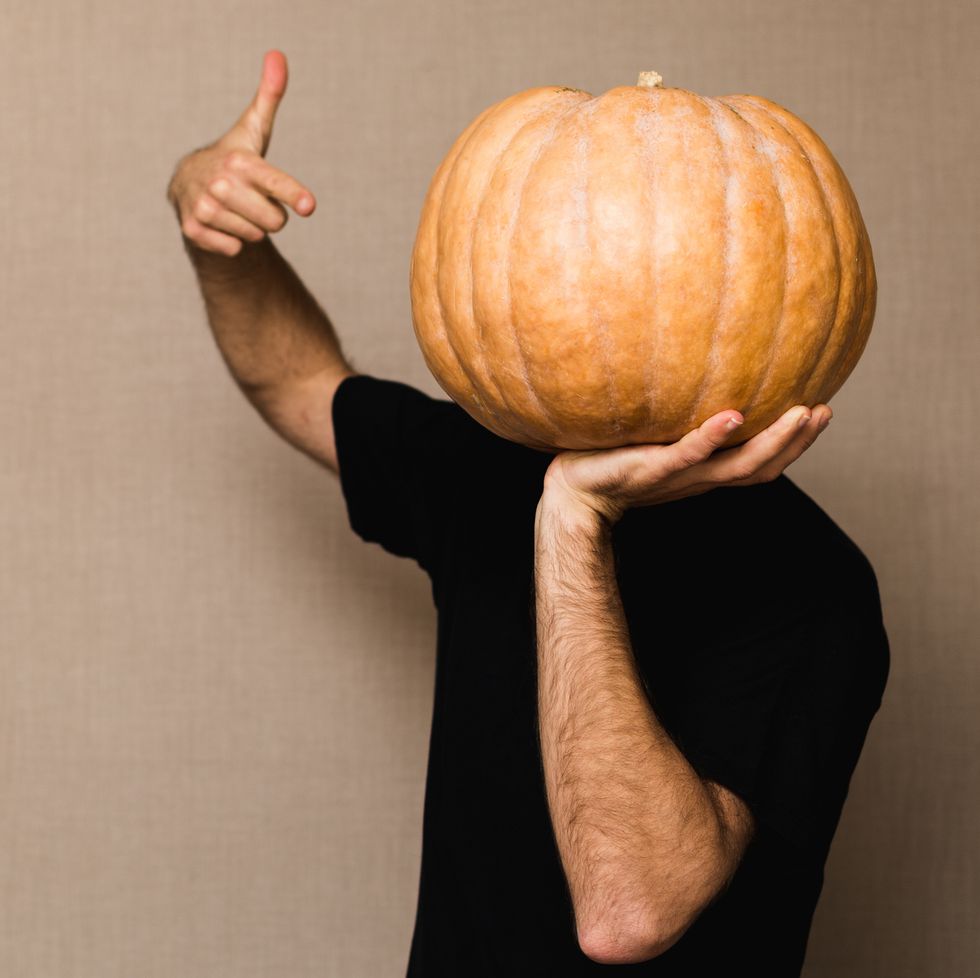 Young man in black t-shirt holding big pumpkin in front of his face
