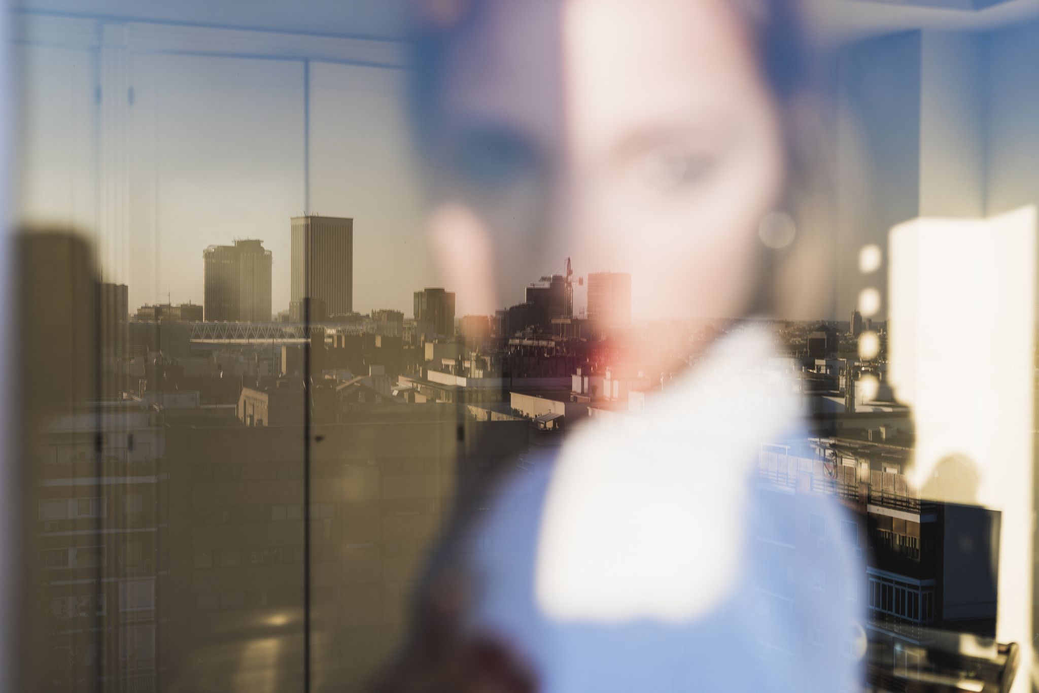 Spain, Madrid, blurred view of woman behind windowpane with reflection of the city