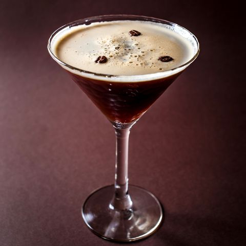 glass of espresso martini with coffee beans and vodka on elegant dark brown background