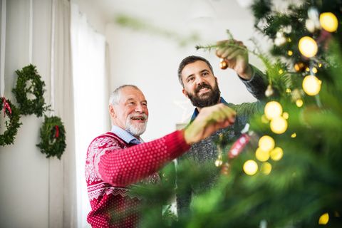 a happy senior father and adult son decorating a christmas tree at home