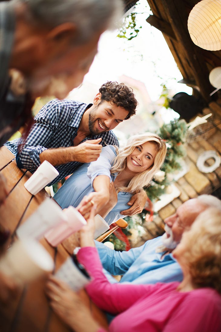 closeup of a mid 20's couple revealing to their parents that they are engaged by showing engagement ring on future bride's finger