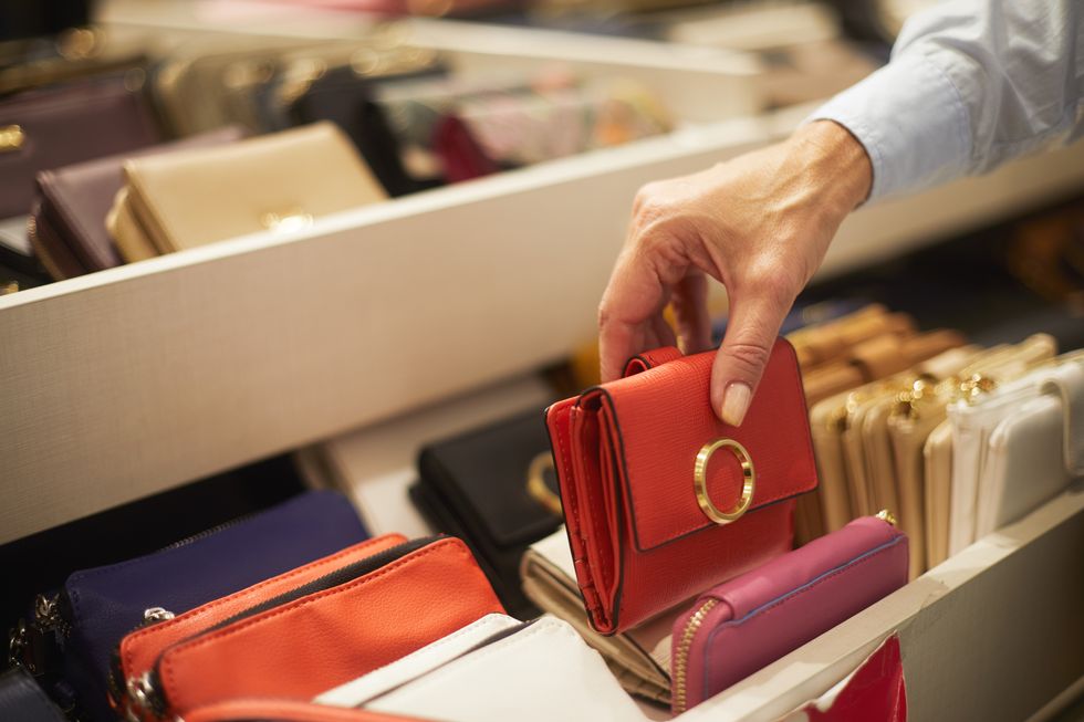 a close up of a small red wallet being picked up from a rack in a bags and wallets store