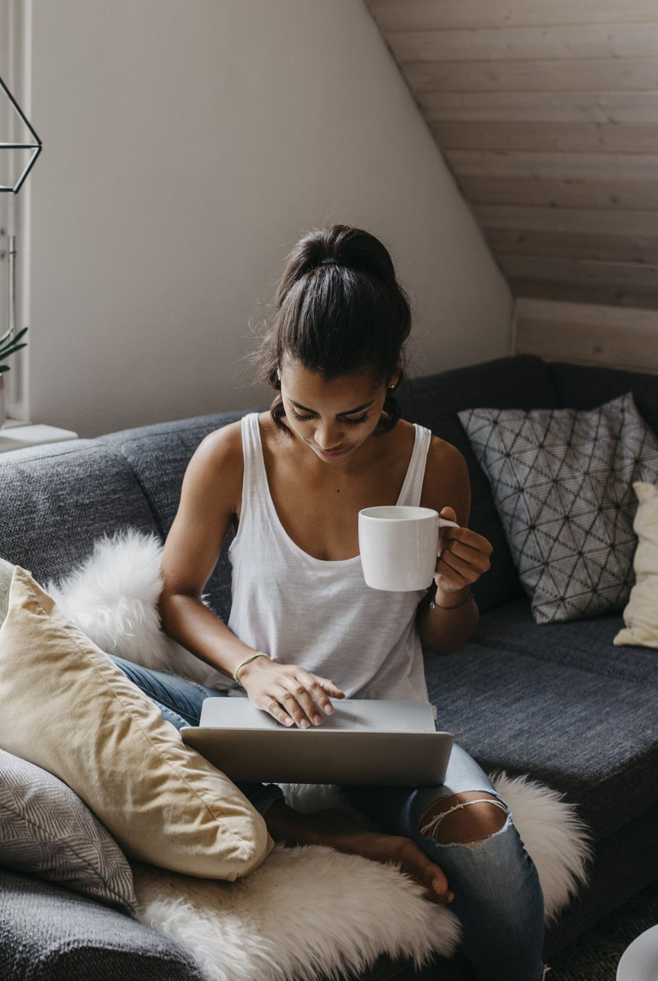 young woman sitting on the couch with cup of coffee using laptop