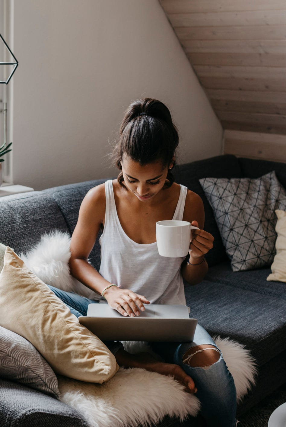 young woman sitting on the couch with cup of coffee using laptop