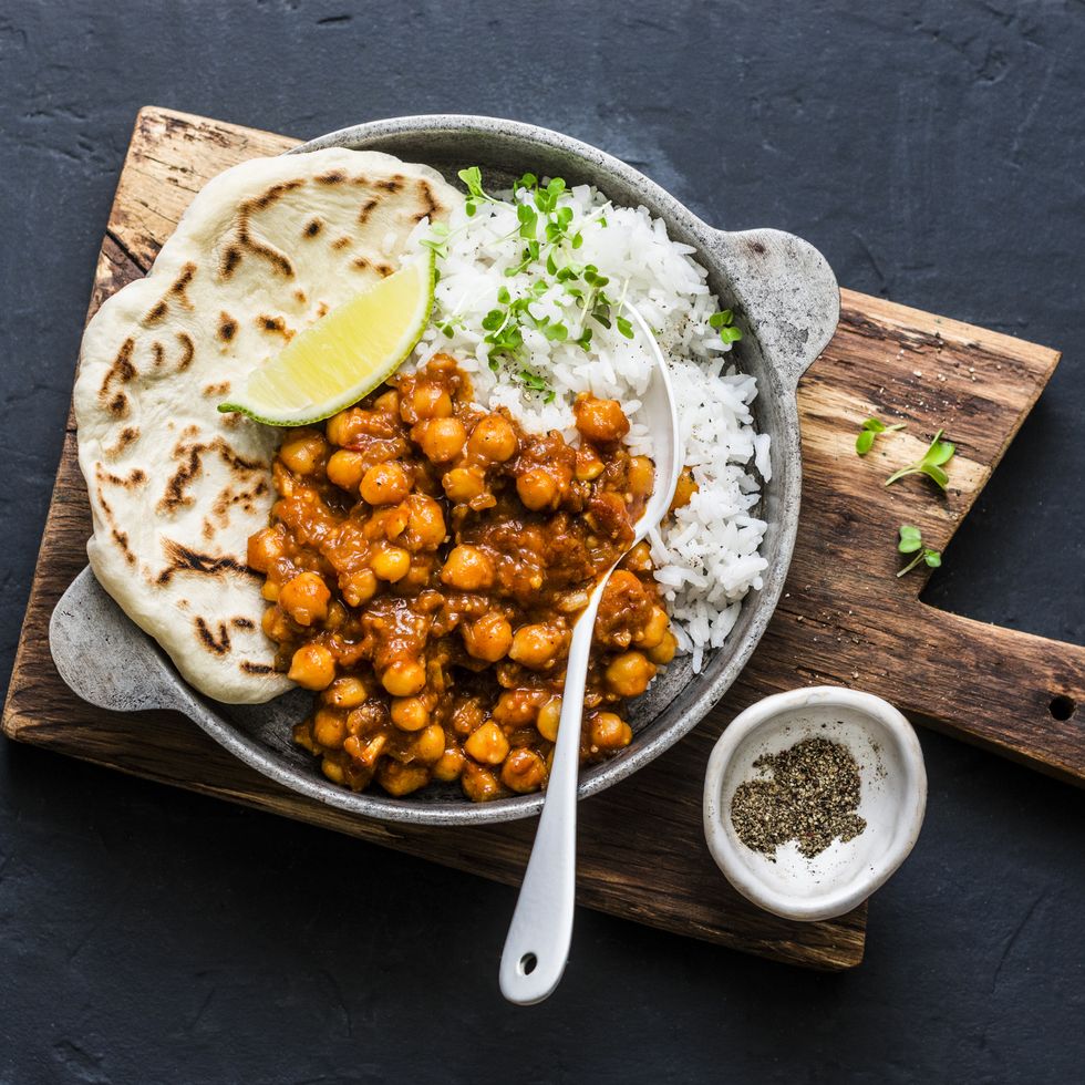 Indian spicy chickpeas curry with rice and naan bread in pan on dark background, top view. Healthy tasty vegetarian food