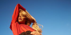 portrait of beautiful young woman with long blond hair wearing red blouse and black pants dancing on meadow shot from low angle view perspective