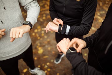 group of people looking at their fitness trackers smartwatch after their run in the park close up of young men and women using their smartwatches after sports training