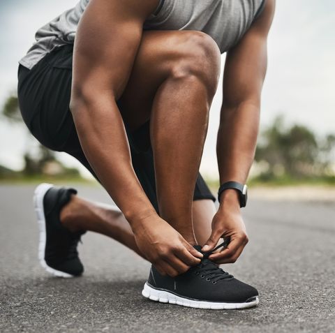 closeup shot of a sporty man tying his shoelaces while exercising outdoors