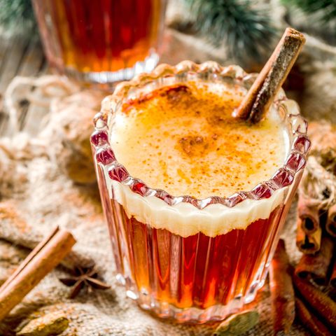winter holidays traditional drink, homemade hot buttered rum with spices, over old rustic wooden background with christmas tree branches, copy space