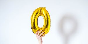 a young person is holding a golden colored number zero on a white background