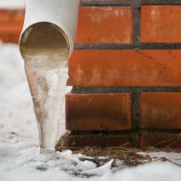 drain pipe with frozen stream of water near brick wall of a cottage outdoors in winter