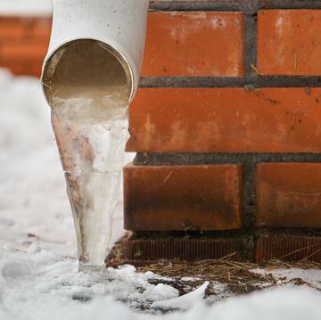 drain pipe with frozen stream of water near brick wall of a cottage outdoors in winter