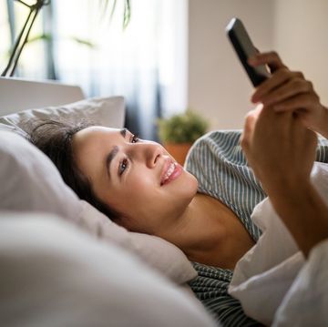 young woman lying in her bed and using smart phone woman waking up in her bed and checking her phone