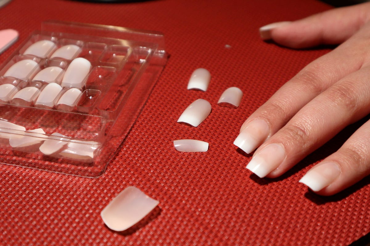 several press on nails and a hand with press on nails applied on a red background