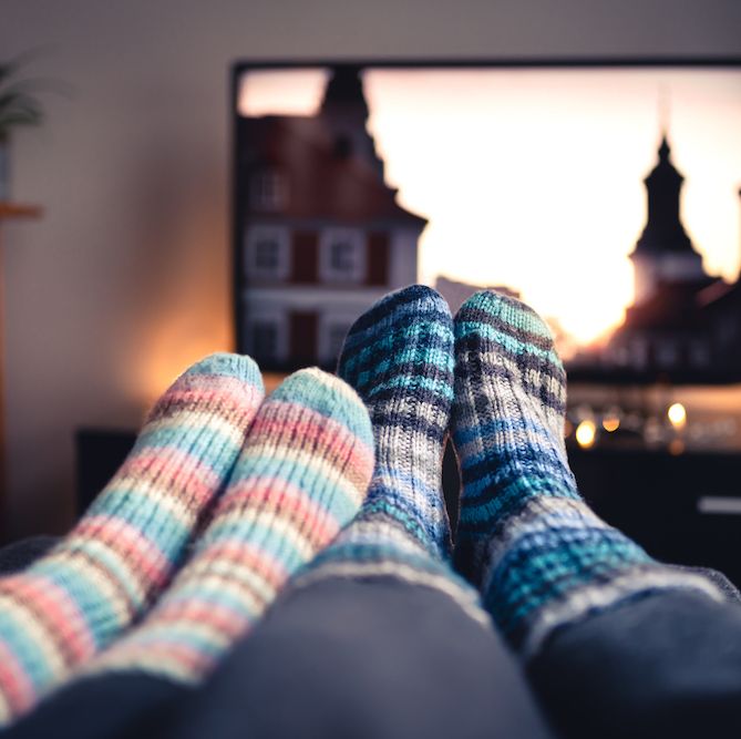 Couple with socks and woolen stockings watching movies or series on tv in winter. Woman and man sitting or lying together on sofa couch in home living room using online streaming service.