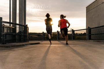 Two runners in active wear jogging on a rooftop at sunset