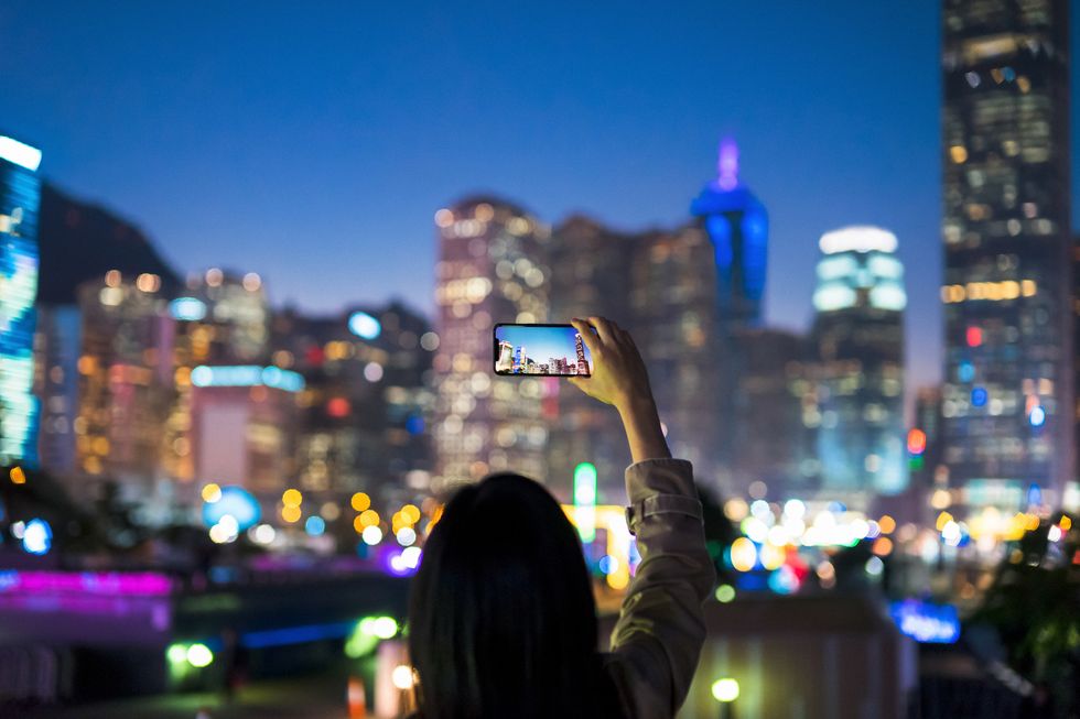 young woman using a smartphone to capture the spectacular and colourful night view of hong kong cityscape