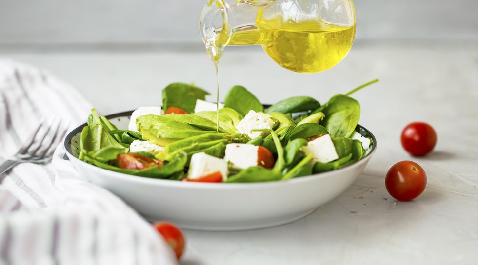 Pouring olive oil in healthy green vegetables and cheese salad, healthy eating mediterran diet concept, feta cheese and avocado salad with spinach , tomatoes and lettuce bowl with olive oil bottle