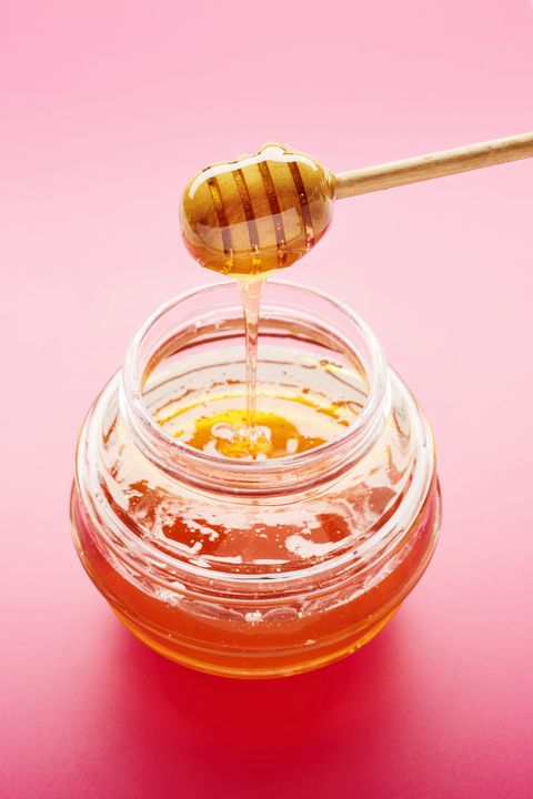 Honey dipper with liquid honey in jar on pink background