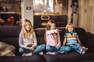 small happy siblings relaxing on sofa at home and changing channels on tv