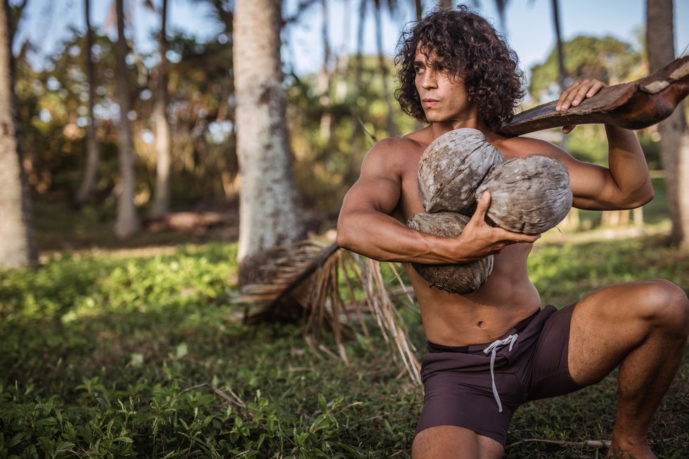 one man, handsome shirtless man holding coconuts and coconut tree branch in nature