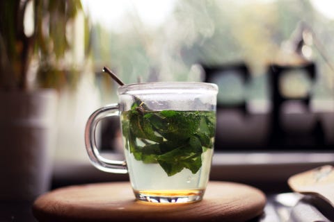 fresh mint tea, with mint leaves and honey, in a glass cup stood on wooden board by a kitchen window plant in the background a cafe sign is also in background, partly covered