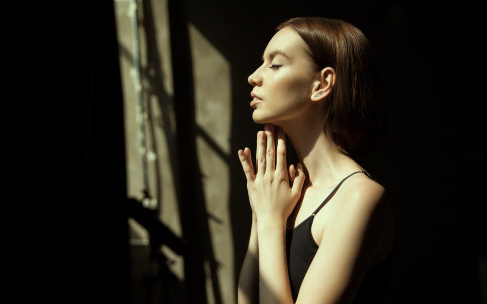 attractive young lady in stylish outfit looking away while standing in dark room