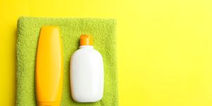 green terry towel and sunscreen on bright yellow background concept hygiene, body care top view, copy psace