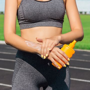 young female runner standing and putting sun lotion on hand girl using sunscream before sport running exercise on summer morning sports and healthy concept