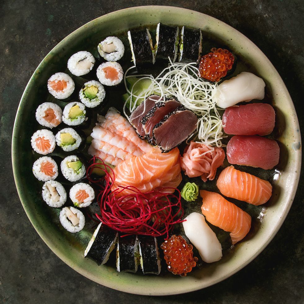 sushi set nigiri sashimi and sushi rolls in ceramic serving plate with salad over dark metal texture background flat lay, space japan menu