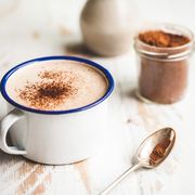 a warm cup of hot chocolate, on a rustic white washed timber table top, flanked by a small handmade vase of lavender leaves