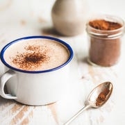 a warm cup of hot chocolate, on a rustic white washed timber table top, flanked by a small handmade vase of lavender leaves